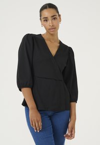 Černý top s balónovými rukávy po tři �čtvrtiny, texturovaná látka a výstřih do V. Spárován s modrými skinny džíny. Jednoduchý design pro univerzální nošení.