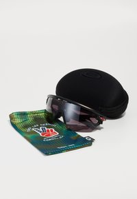 Sonnenbrille mit schwarzem Rahmen und getönten Gläsern, begleitet von einem Mikrofasertäschchen mit grünem Camouflage-Muster und einem schwarzen Schutzhülle.