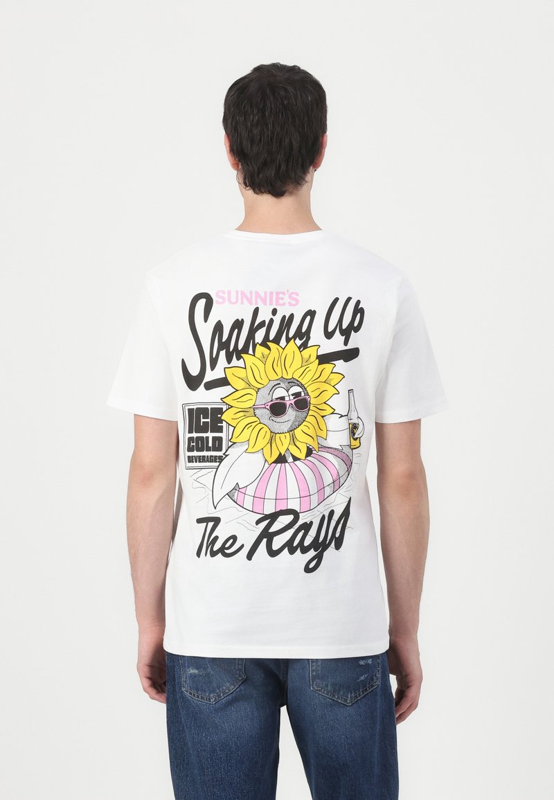 T-shirt en coton blanc avec un imprimé graphique coloré d'un tournesol portant des lunettes de soleil, avec le texte "Sunnie's Soaking Up The Rays" et des accents.