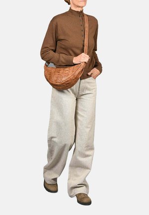 Bruine, gestructureerde schoudertas in een halve maanvorm; gedragen met grijze broeken en een bruine, knooptop. Eenvoudige, platte schoenen maken de look compleet.