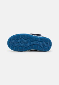 Suela de zapato deportivo con material de goma azul, superficie texturizada y patrón en zigzag para tracción. Presenta bordes reforzados y marcas de la marca.