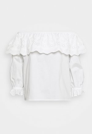 Blusa blanca de algodón sin hombros con un diseño de ojales con volantes, mangas largas con puños elásticos y un corte holgado.