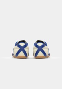 Adidași alb-albaștri cu un superior din piele netedă, accente cusute în cruce, căptușeală gri și talpă din cauciuc caramel. Vedere din spate.