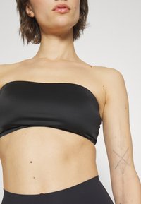 Čierny bandeau top vyrobený z hladkej, elastickej látky; priliehavý dizajn bez ramienok, s čistým, jednoduchým výstrihom a lemovaním.