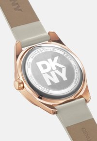 Ronde horloge met een roestvrijstalen kast en een roségouden afwerking. Beschikt over een grijze wijzerplaat, een lichtgrijze leren band en een kroon aan de zijkant.