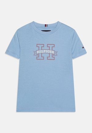 Hellblaues T-Shirt mit kurzen Ärmeln mit rotem umrandetem "H" und dem Schriftzug "HILFIGER" auf der Brust, mit kleinem Flaggenlogo am Ärmel.