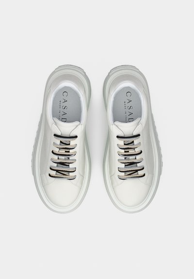 Άσπρα sneakers χαμηλής κοπής με γκρι και μαύρα κορδόνια, χοντρές ανοιχτογκρι σόλες και επάνω σόλες με τη μάρκα που γράφουν «CASADEI Made in Italy».