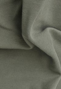 Getextureerde groene stof met een licht grove weving, met zachte plooien en subtiele schaduwwerking, geschikt voor kleding of bekleding.