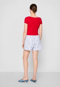 Rød tilpasset t-skjorte med korte ermer, kombinert med lyseblå stripete shorts med rød stjernebroderi og blå slip-on sandaler.