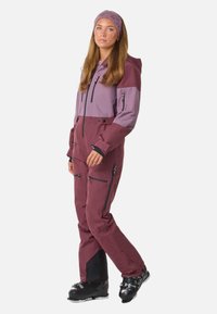 Ski overall in bordeaux en lavendel, met ritszakken, een capuchon en zwarte accentdetails. Beschikt over een aansluitend ontwerp voor wintersport.