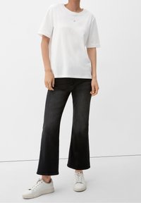 Biała, krótki rękaw t-shirt z małym czerwonym okręgiem, zestawiony z czarnymi spódnicami dzwonowymi i białymi trampkami.