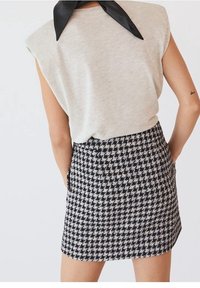 Femme portant une minijupe à motif pied-de-poule noir et blanc et un haut beige sans manches avec un col noir, vue de dos.