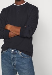 Sudadera azul marino con cuello redondo, puños acanalados y un acabado texturizado, combinada con unos vaqueros de denim azul claro.