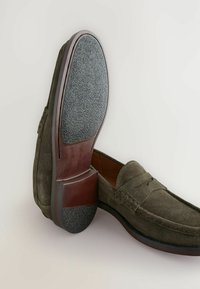 Donkergroene suède instappers met een platte rubberen zool, een afgeronde neus, contrasterende bruine leren accenten en een gestructureerde voetbed.