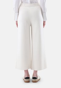 Weite Hosen aus cremefarbigem Stoff mit glatter Textur und hohem Bund. Die Rückansicht zeigt subtile Nahtdetails und Taschen.