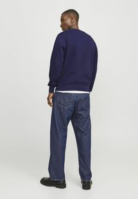 Sudadera azul marino con puños y dobladillo acanalados, combinada con vaqueros rectos de un azul oscuro. Zapatos negros completan el conjunto.
