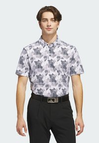 Kurzarm-Golf-Polohemd in einem weißen und grauen geometrischen Muster, mit Kragen und Knopfleiste, kombiniert mit schwarzen Hosen und einem Gürtel.