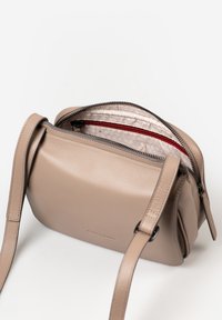 Beige Leder Umhängetasche mit Reißverschluss, Innentasche und verstellbarem Trageriemen; glatte Textur mit abgerundeten Kanten.