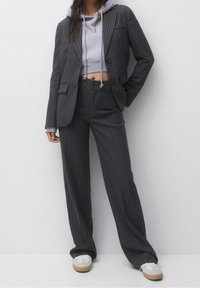 Traje gris a rayas con una chaqueta entallada y pantalones de pierna ancha, superpuesto a una sudadera corta gris y combinado con zapatillas blancas.