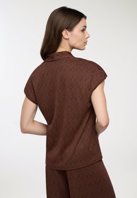Top marrone a fantasia con maniche corte e una texture morbida, caratterizzato da un design geometrico e un colletto sottile, mostrato di spalle.