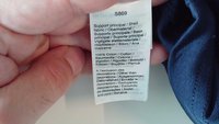 Ruka drži oznaku za odjeću na kojoj je sastav tkanine 100% pamuk na više jezika i oznaka proizvoda S869.