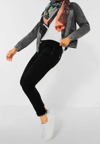 Vaqueros pitillo negros con una cinturilla alta, decorados con botones metálicos a los lados. Combinados con una chaqueta gris claro y una bufanda estampada.