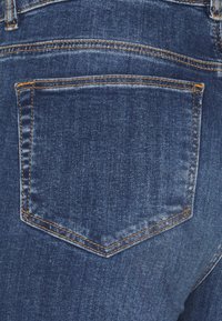 Mörkblå denimjeans med en delvis synlig bakficka, prydd med orange sömnad och en slät yta.