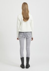 Vit vadderad jacka med kort skärning, i kombination med ljusgrå skinny jeans och svarta kraftiga stövlar. Vågtigt långt hår är delvis synligt.