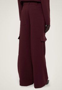 Bordeaux wijde cargobroek van zachte stof, met grote zijzakken en een gladde textuur. Aangepaste pasvorm met een riemlus.