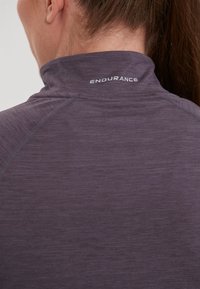 Purple athletic top with a high collar, featuring a smooth texture and flatlock seams. "ENDURANCE" logo printed at the collar.