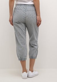 Pantalons cropped en mélange de coton avec un motif rayé vertical bleu et blanc, taille élastique et poignets resserrés ; portés avec des baskets blanches.