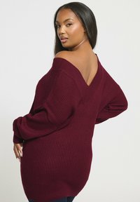 Burgundowa sweter z prążkowanego materiału z otwartymi plecami i oversize'owymi rękawami, z głębokim dekoltem w serek i luźnym krojem.