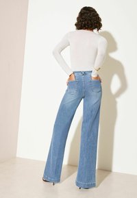 Hellgraues Langarmshirt kombiniert mit hochtaillierten, weit geschnittenen hellblauen Jeans mit Gesäßtaschen und einem sauberen Finish.