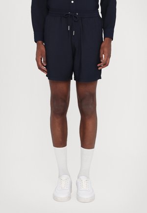 Shorts de bain bleu marine avec une taille élastique et un cordon de serrage, poches latérales, coupe décontractée, portés avec des chaussettes blanches et des baskets.