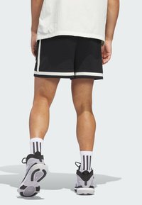 Black athletic shorts with white trim, mesh texture. Worn with striped white socks and gray sneakers. View from the back, showing legs.