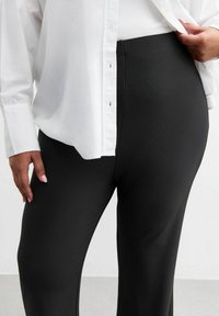 Pantalones negros de canalé con cintura alta, hechos de material elástico. Combinados con una camisa blanca suelta con botones.