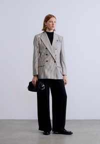 Γκρι και λευκό καρό διπλόσαρκο σακάκι με μαύρα κουμπιά, σε συνδυασμό με φαρδιά μαύρη παντελόνια και μια μικρή μαύρη τσάντα χειρός.