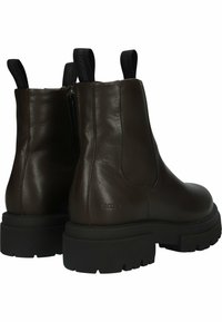 Botas de cuero marrón hasta el tobillo con suela negra gruesa, cremallera lateral y tiradores para facilitar el uso. Textura suave y diseño minimalista.