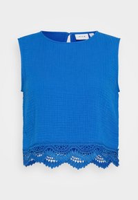 Blå ermeless topp med teksturert stoff, med en scalloped blondekant og en nøkkelhull lukking bak. Merke synlig inne i halslinningen.