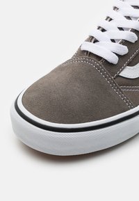 Braune Wildleder-Sneaker mit weißen Schnürsenkeln und einem cremefarbenen Seitenlogo. Verfügt über einen schwarzen Rand um eine strukturierte Gummisohle.