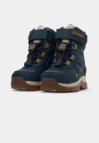 Bottes de randonnée pour enfants en bleu marine et marron avec des sangles Velcro, des lacets élastiques et des semelles texturées sur un fond blanc.