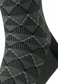 Schwarz und dunkelgrün gemusterte Socke mit geometrischem Design, strukturierten Details und verstärktem Fersenbereich.