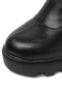 Melnas ādas potītes zābaki ar noapaļotu purngalu, strukturētu virsmu, kontrastējošām šuvēm un biezām gumijas zolēm, kurām ir protektora raksts.