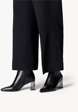 Bottines en cuir noir avec talons blocs transparents portées avec un pantalon noir à jambes larges.