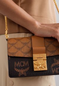 Brown leather handbag featuring a tan patterned flap, gold hardware, and a chain strap. Logo details embossed on the body.