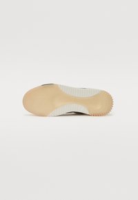 Shoe sole in beige and white with textured grip and tread pattern, photographed from below on a plain white background.