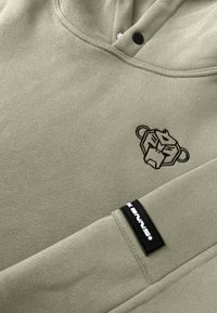 Olijfgroene hoodie met een kangoeroezak, voorzien van een zwart geborduurd leeuwlogo op de borst en een zwart merklabel op de sleeve.