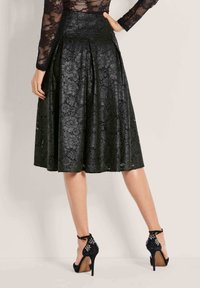 Zwarte kanten rok met een geplooid ontwerp, met een gestructureerde afwerking en een lengte tot halverwege het kuit. Gecombineerd met zwarte hoge hakken.