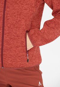 Röd, texturerad fleecejacka med fullängdssdragkedja och sidofickor. Ärmarna och nederkanten är kantade. Bärs med matchande byxor.