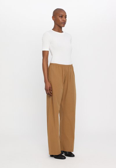 Hvit tettsittende t-skjorte, beige vide bukser med elastisk midje og svarte ankelstøvler. Enkelt design, glatt tekstur og nøytrale farger.